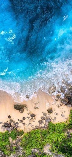 an aerial view of the beach and ocean with rocks, grass and water in the foreground