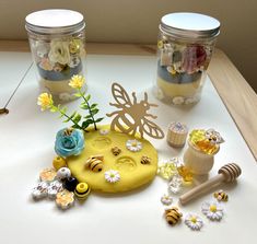 two jars filled with flowers and bees sitting on top of a table next to each other