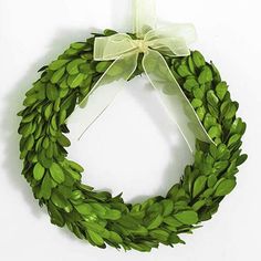 a green wreath hanging on the wall with a bow around it's neck and ribbon