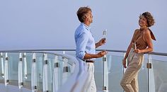 a man and woman standing on top of a balcony next to each other holding wine glasses