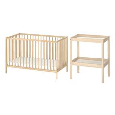 a baby crib next to a night stand with a white sheet on the bottom