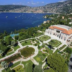 an aerial view of a large mansion with gardens and boats in the water behind it