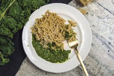 a white plate topped with pasta and spinach next to a gold spoon on top of a table