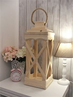 a wooden lantern sitting on top of a white table next to a lamp and flowers