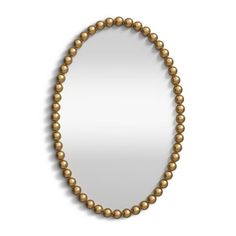 a gold beaded necklace hangs on a white wall with a mirror in the background