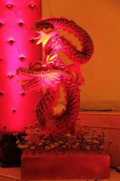 a red dragon sculpture sitting on top of a table next to a planter filled with flowers