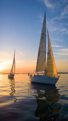 two sailboats in the water at sunset