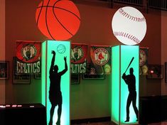 the silhouettes of baseball players and basketball balls are projected on pedestals in an indoor setting