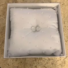 two wedding rings are placed on top of a pillow in a box that is sitting on the floor