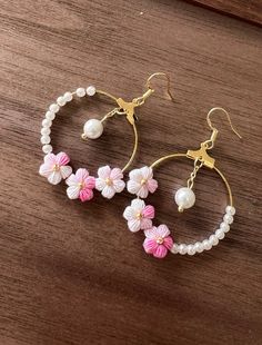 two hoops with flowers and pearls hanging from them on top of a wooden table