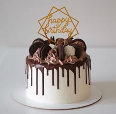 a birthday cake with chocolate icing and cookies on top that has the words happy birthday written in gold