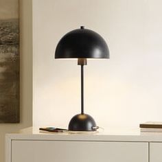 a black lamp sitting on top of a white dresser next to a painting and books