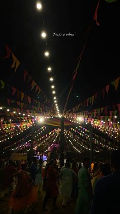 many people are standing in the middle of a long hallway with lights strung from it