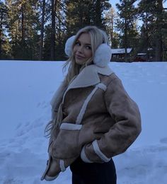 a woman standing in the snow wearing a jacket and hat with ear muffs on her head