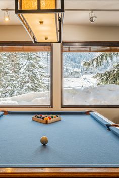 a pool table in front of two large windows with snow on the ground and trees outside