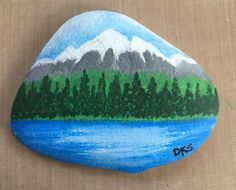 a painted rock with trees and mountains on it