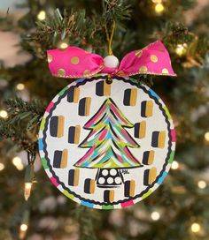 a christmas ornament hanging from a tree with lights in the background and a pink bow on it