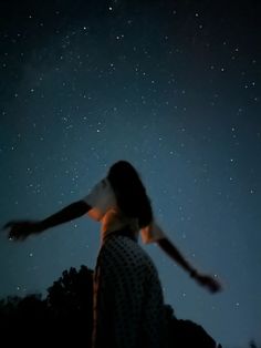 a person standing in the dark with their arms spread out to the stars above them