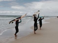 three surfers carrying their boards into the water at the beach on a cloudy day