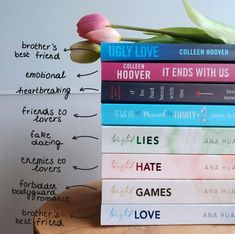 a stack of books sitting on top of a wooden table next to a pink tulip