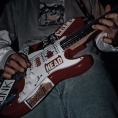 a man holding a red and white guitar in his right hand with the word head on it