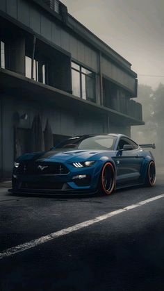 a blue mustang parked in front of a tall building on a foggy day with orange rims