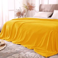 a bed covered in a yellow blanket next to a vase with flowers on top of it