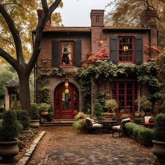 an old brick house with red doors and shutters on the windows is surrounded by greenery