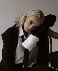 a woman sitting on top of a wooden chair wearing a black suit and white shirt