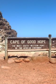 a wooden sign sitting on the side of a dirt road next to some rocks and grass