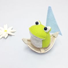 a green frog sitting on top of a wooden sled next to a white flower