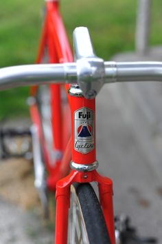 the front end of a red bicycle parked in a parking lot next to a grassy area