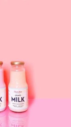 two bottles of milk sitting next to each other on a pink surface with the word milk written in gold