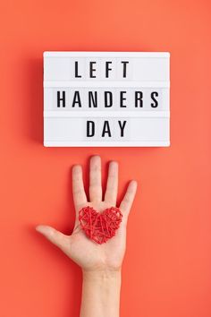 a hand with a string heart in front of a sign that says left handeders day