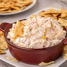 a red bowl filled with dip and chips on top of a white plate next to some crackers