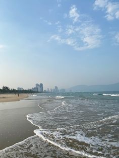 the beach has waves coming in to shore and buildings in the distance with blue sky