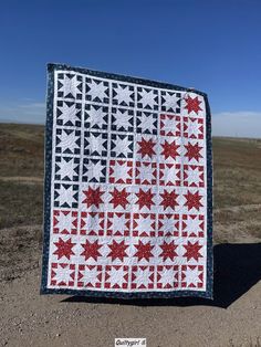 a red and white quilt sitting on top of a dirt field