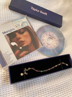 a box with a cd, necklace and other items in it sitting on a bed