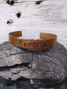 a leather bracelet with the word fierce on it sitting on top of a rock in front of a white brick wall