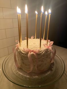 a birthday cake with white frosting and pink bows on top is sitting on a glass platter