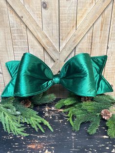 two green bows with pine cones and evergreen needles on the side of a wooden wall