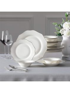 a table set with white dishes and silverware, wine glasses and flowers in vase