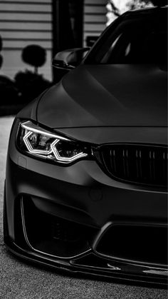 the front end of a black car parked in a parking lot next to a garage