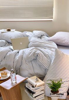 a laptop computer sitting on top of a bed covered in blue and white striped sheets