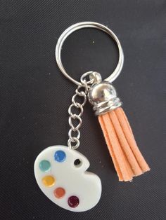 a keychain with a paint palette on it and a tassel in the shape of a heart