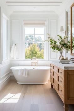 a white bath tub sitting under a window next to a sink and a wooden cabinet