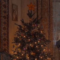 a small christmas tree is lit up in front of a window with gold stars on it