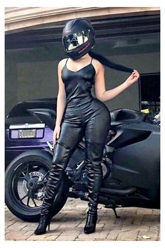 a woman in black leather outfit and helmet standing next to a motorbike on the street