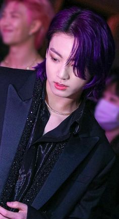 a woman with purple hair wearing a black suit and silver necklace, looking down at her cell phone