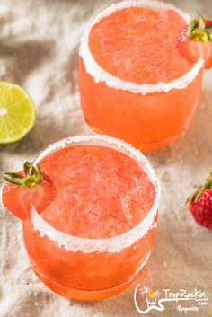 two margaritas are garnished with strawberries and lime on a tablecloth